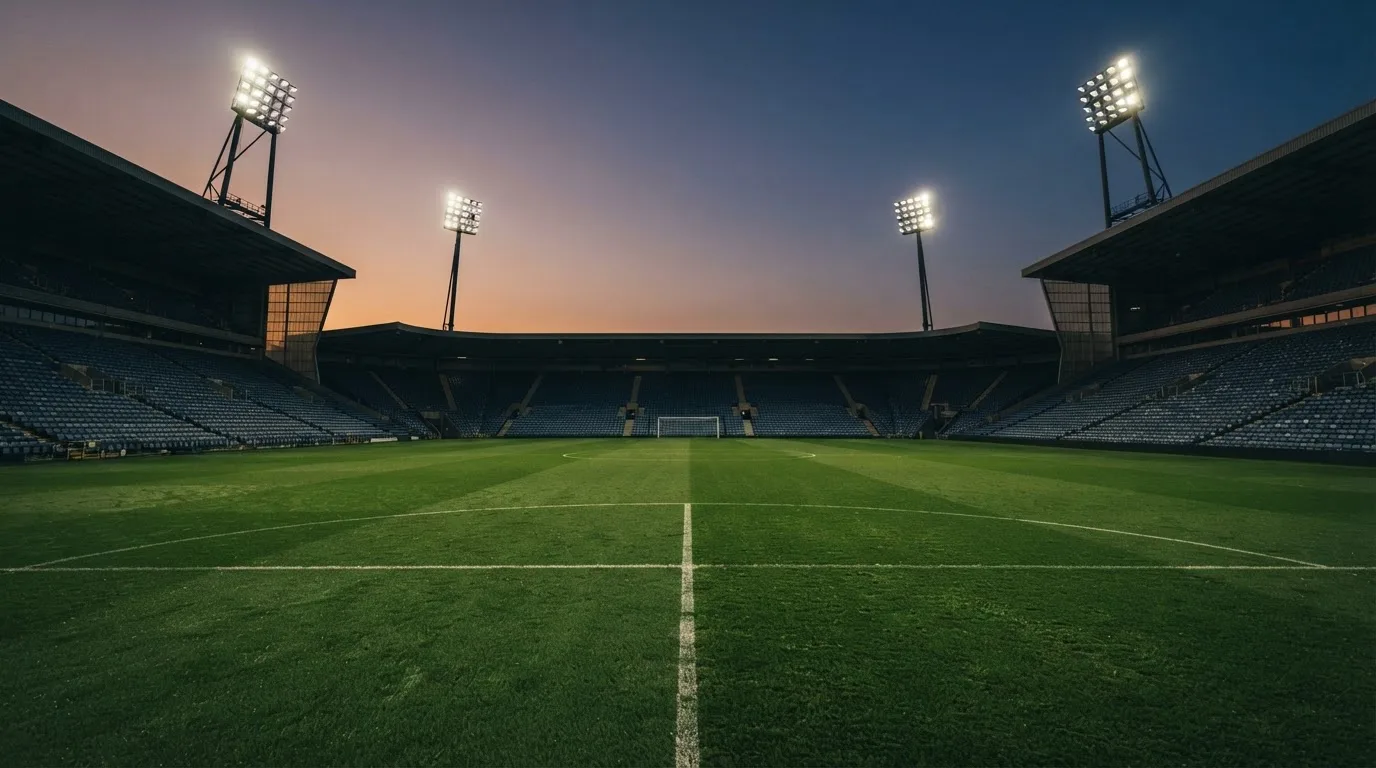 An empty football stadium with floodlight masts at dusk