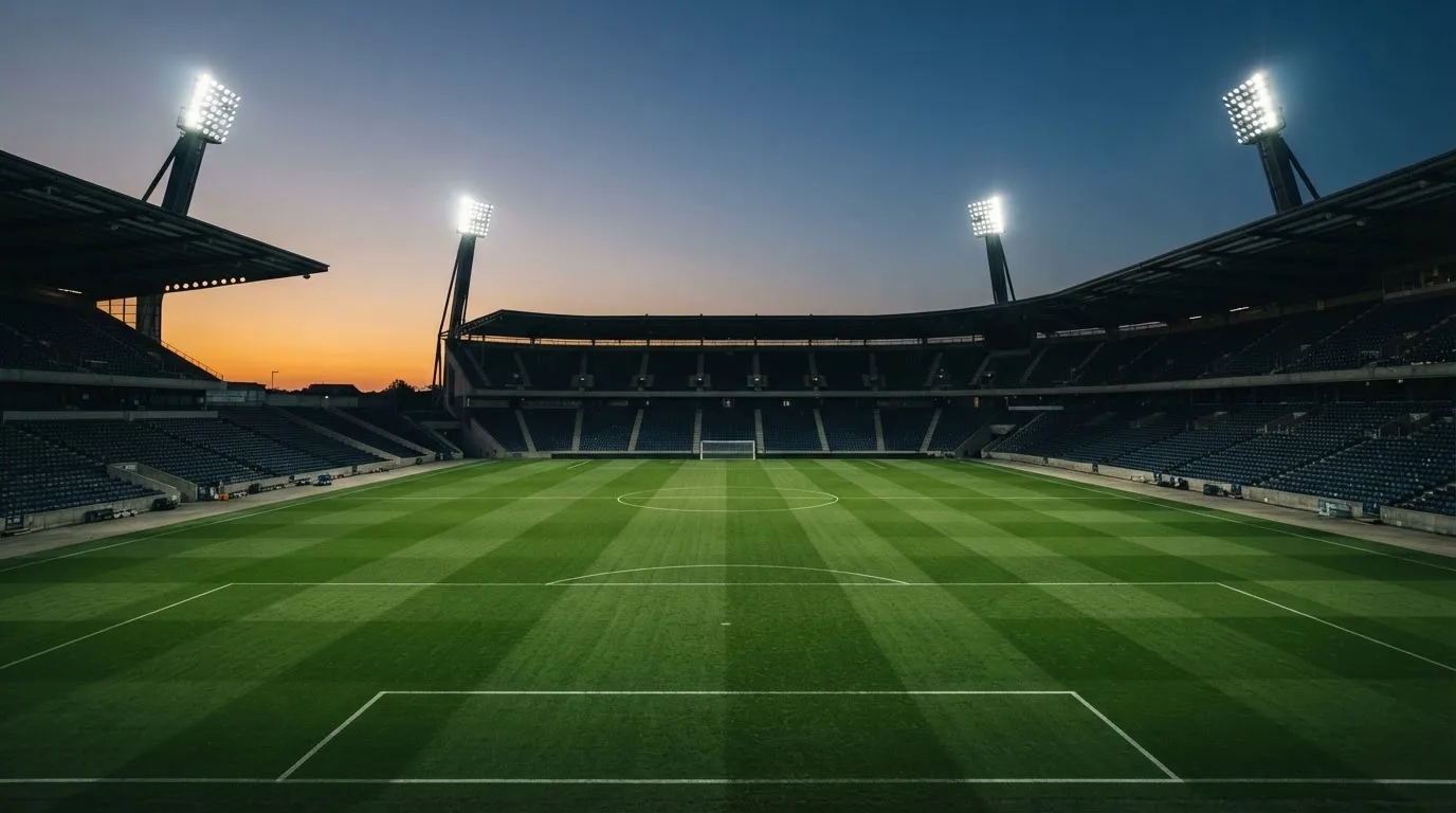 An empty football stadium with floodlight masts at dusk