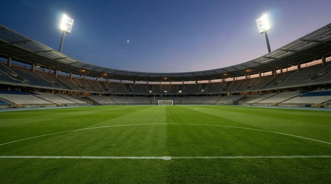 An empty football stadium with floodlight masts at dusk