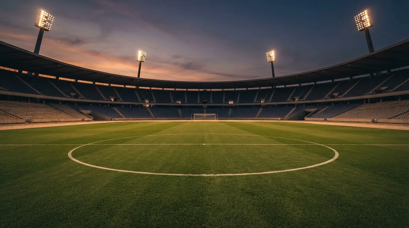 An empty football stadium with floodlight masts at dusk