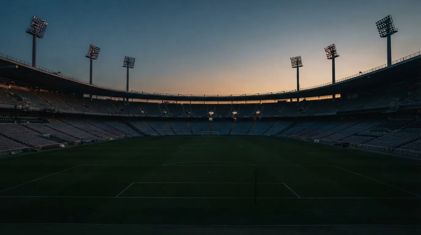 An empty football stadium with floodlight masts at dusk
